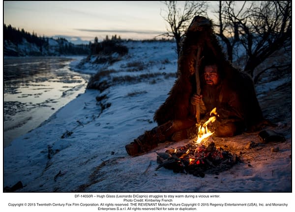 A dramatic scene from "The Revenant" shows Hugh Glass, portrayed by Leonardo DiCaprio, seeking warmth by a small fire in a snowy landscape during a harsh winter.