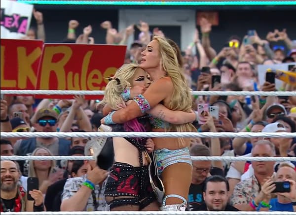 Charlotte Flair and Alexa Bliss embrace in celebration after winning the tag team title at WWE SummerSlam. A cheering crowd is visible in the background, holding signs and phones.