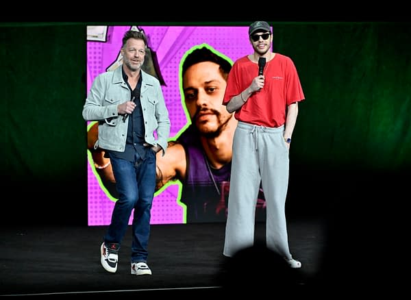 David Leitch and Pete Davidson speak onstage at CinemaCon 2026 in front of a colorful poster for How To Rob A Bank.