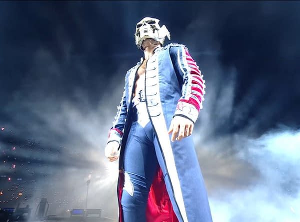 Cody Rhodes makes a dramatic entrance, wearing a flashy coat and a skull mask, under bright lights with fog effects in the background. The atmosphere is charged as he approaches the ring, symbolizing his challenge for the WWE Championship.