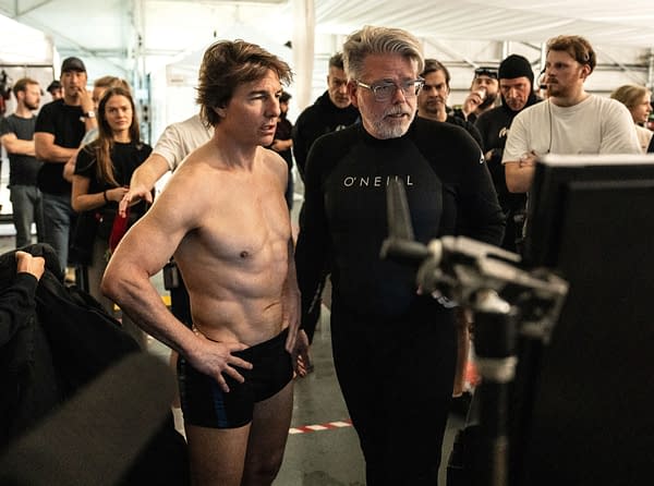 Behind-the-scenes photograph from 'Mission: Impossible - The Final Reckoning' featuring Tom Cruise shirtless alongside director Christopher McQuarrie, both focused on a monitor as crew members observe.