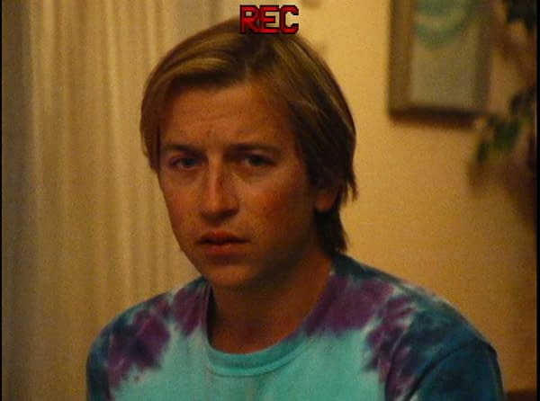 A close-up, grainy shot of a serious young man in a tie-dye shirt indoors, with a red REC indicator at the top.