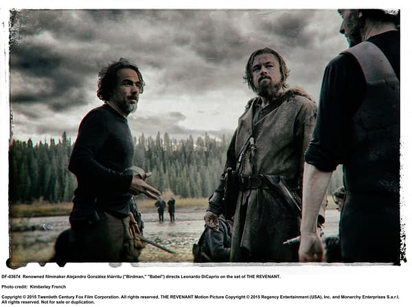 Behind-the-scenes photo of director Alejandro González Iñárritu discussing a scene with actor Leonardo DiCaprio on the set of 'The Revenant.' A dramatic sky and wooded background add to the intense atmosphere.