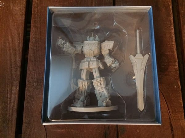 The Megazord deluxe figure component for Renegade Game Studios' Power Rangers: Heroes of the Grid board game, in its box behind plastic. It even comes with a neat sword!