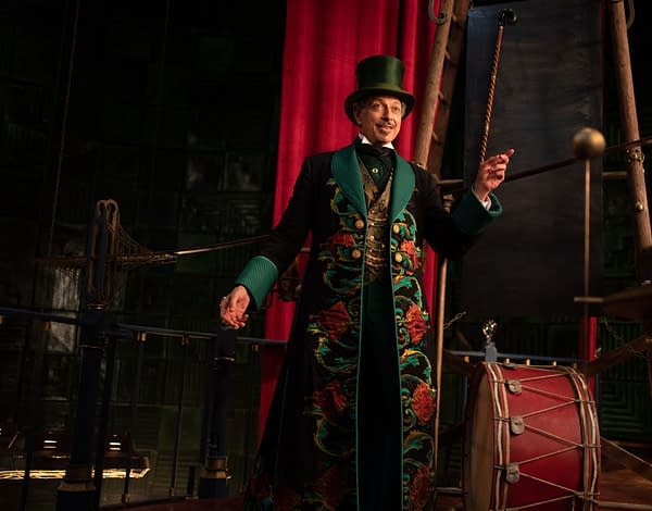 Jeff Goldblum portrays The Wizard of Oz in the musical 'Wicked: For Good,' wearing an elaborate, floral-patterned coat and top hat, with a theatrical backdrop visible behind him.