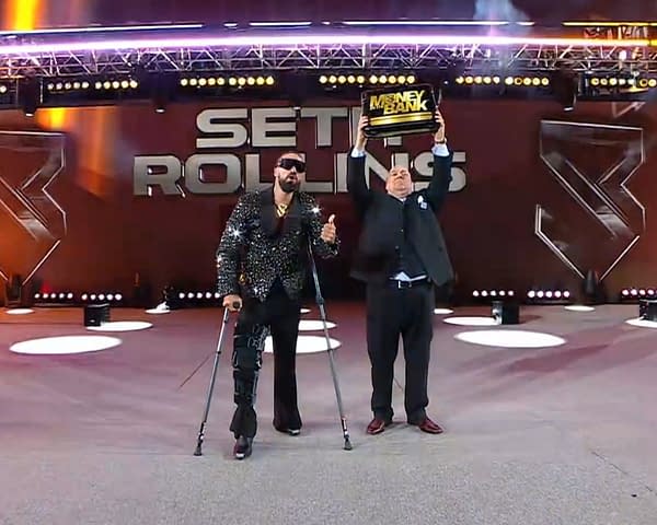 A man wearing a sparkling outfit and using crutches, Seth Rollins, stands on a wrestling ramp, giving a thumbs-up while another man, manager Paul Heyman, in a suit, raises a Money in the Bank briefcase above his head.