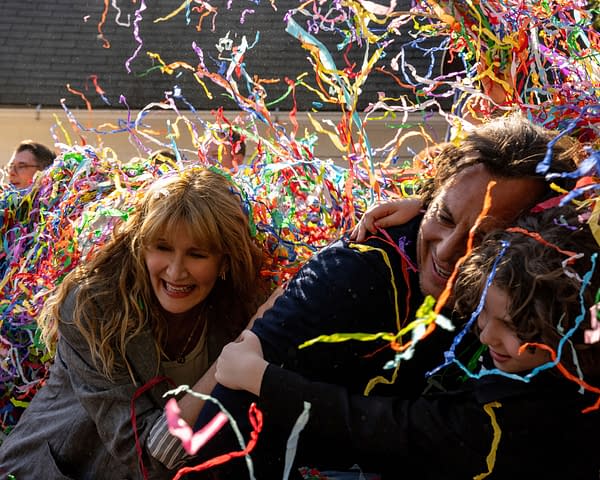 A joyful scene from the film "IS THIS THING ON?" featuring Laura Dern, Will Arnett, and Calvin Knegten amidst colorful confetti and streamers. The trio is engaged in a playful embrace, conveying a festive and cheerful atmosphere.