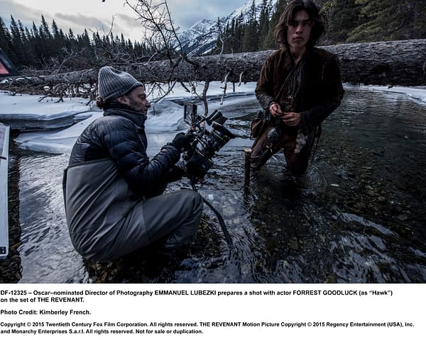 Oscar-nominated Director of Photography Emmanuel Lubezki sets up a camera shot with actor Forrest Goodluck, who plays Hawk, on the set of 'The Revenant,' surrounded by a scenic, natural backdrop.