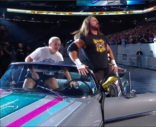 AJ Styles confidently makes his entrance for a match against Dominik Mysterio at WWE SummerSlam, showcasing a stylish look with a classic car backdrop in a tribute to Eddie Guererro. His companion, dressed in casual attire, appears excited as they approach the ring.