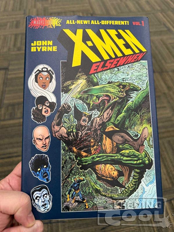 A person holds a comic book titled 'X-Men: Elsewhen' featuring colorful illustrations of various characters, including Storm and Cyclops, along with a dramatic scene with a large creature. The cover includes bold yellow and red lettering and the name 'John Byrne.'