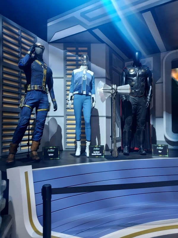 Marvel costume display at SDCC showing three mannequins in superhero outfits, including a blue suit, a Fantastic Four costume, and Thor armor beside a large prop axe.