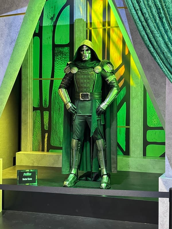 Doctor Doom costume display at SDCC, with a hooded armored figure standing on a green-lit stage.