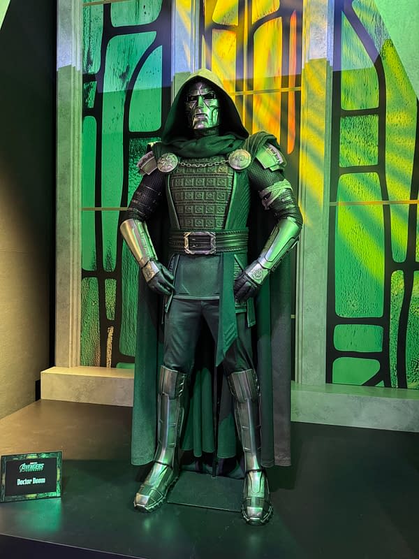 Doctor Doom costume on display at San Diego Comic-Con, with a hooded armored figure standing against a green-and-yellow backdrop.