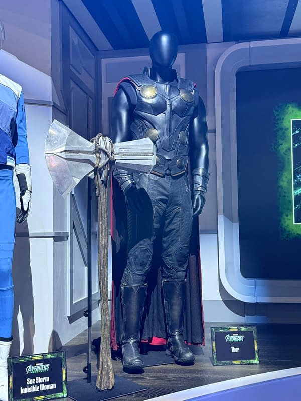 Thor costume display from Avengers: Doomsday at SDCC, featuring a black armored suit, cape, and oversized battle axe on a convention stage.