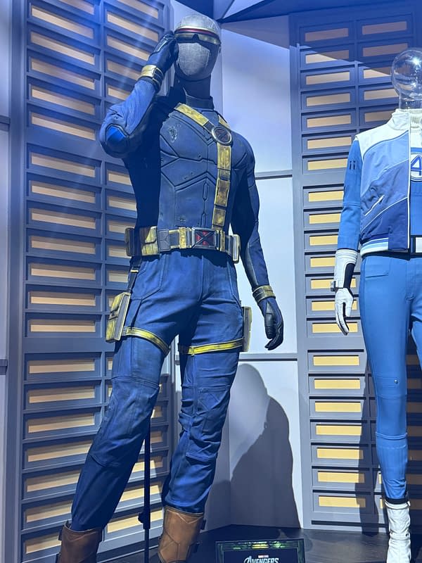 Life-size X-Men costume display featuring a blue-and-gold uniform with a helmeted figure saluting, shown beside a second blue-and-white suit at SDCC.