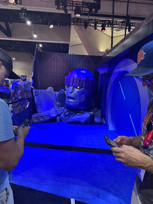 A giant Sentinel head prop glows blue at the Avengers: Doomsday booth at SDCC, with convention attendees standing nearby and taking photos.