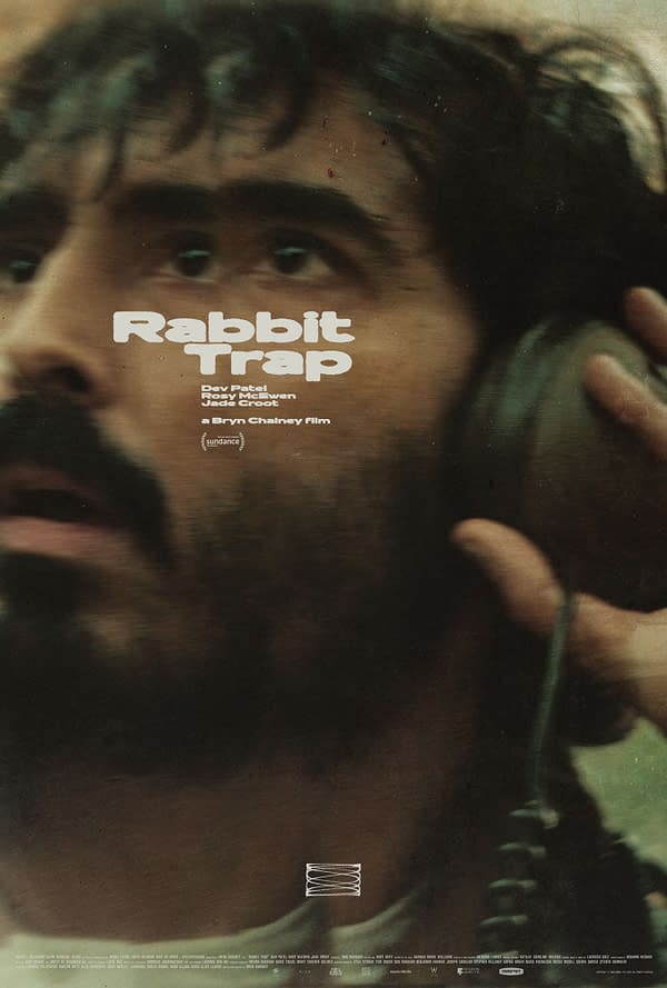 A movie poster for 'Rabbit Trap,' featuring a close-up of a man with dark hair and facial hair, looking intensely at the viewer while holding a headset. The poster includes the names of actors Dev Patel, Rosy McEwen, and Jade Croot, along with the film's title in bold white font.