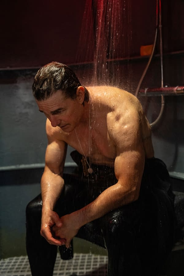 A muscular man is seated under a water shower in a dimly lit setting, with water splashing down on him, conveying a tense or contemplative moment. This scene is from the film 'Mission: Impossible - The Final Reckoning'.