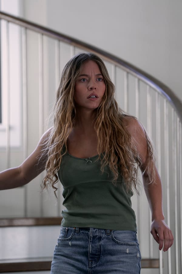Sydney Sweeney portrays Millie Calloway in a tense moment, wearing a green tank top and denim shorts, with long, wavy hair and an expression of concern as she navigates a spiral staircase.