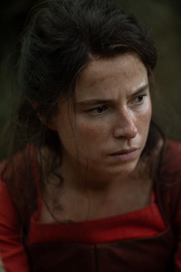 Close-up of Jessie Buckley portraying Agnes, wearing a red dress and appearing contemplative, from the film HAMNET directed by Chloé Zhao.